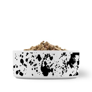 Puede incluir: Taz&oacute;n de cer&aacute;mica blanco para mascotas con un dise&ntilde;o de pintura salpicada negra. El taz&oacute;n est&aacute; lleno de comida seca para mascotas.