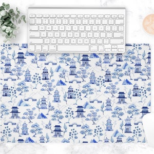 May include: A white and blue desk mat featuring a repeating pattern of pagodas, trees, and bridges. The design is reminiscent of traditional Asian art. A white keyboard and mouse are on top of the mat.