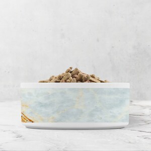 K&ouml;nnte beinhalten: Eine wei&szlig;e Keramik-Tierschale mit einem hellblauen Marmormuster. Die Schale ist mit braunem Tierfutter gef&uuml;llt.