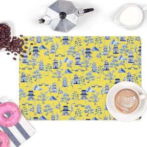 May include: A yellow placemat with a blue and white pattern of Chinese pagodas, trees, and mountains.