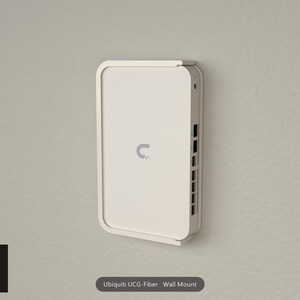 May include: A white wall mount for a Ubiquiti UCG-Fiber device. The mount features a rectangular frame with rounded corners that secures the device against the wall, exposing the side panel with multiple ports and a power input connection.