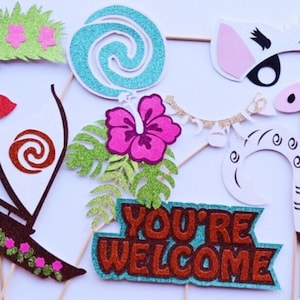 Puede incluir: Un conjunto de 11 accesorios para cabina de fotos con tem&aacute;tica de Moana. Los accesorios est&aacute;n hechos de cartulina con brillantina y presentan personajes y objetos de la pel&iacute;cula, incluyendo una flor, un barco, un cerdo, un gallo y un cartel que dice "Bienvenido".