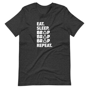 May include: Dark grey t-shirt with white text that reads "Eat. Sleep. BRAP. BRAP. BRAP. Repeat."  The word "BRAP" is repeated three times and each time has a stylized image of a rotary engine.