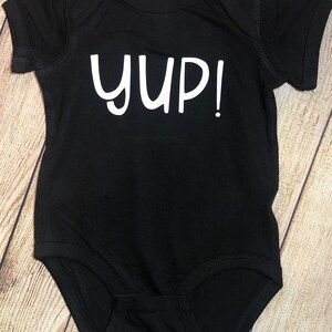 Peut inclure: Combinaison noire pour b&eacute;b&eacute; avec le texte blanc "YUP!"