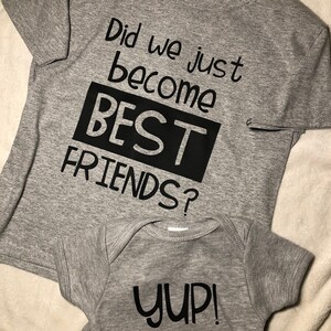 Peut inclure: Deux t-shirts gris avec du texte noir. Le plus grand t-shirt dit "Did we just become BEST FRIENDS?" Le plus petit t-shirt dit "YUP!"