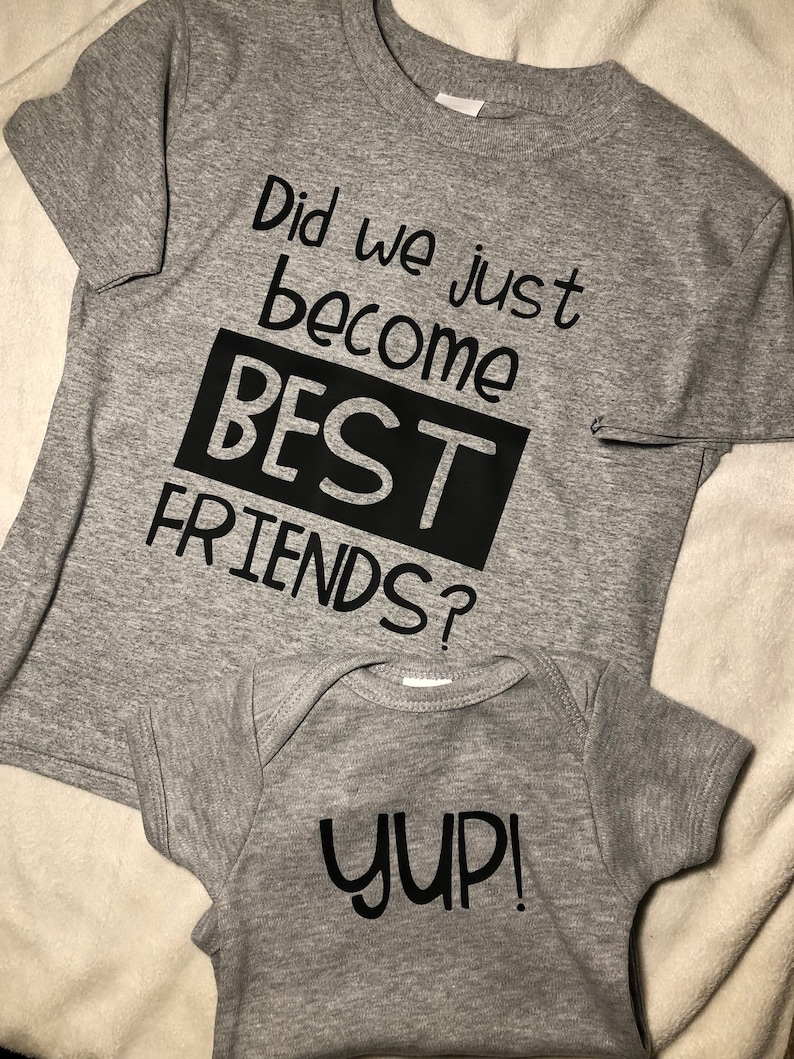 Peut inclure: Deux t-shirts gris avec du texte noir. Le plus grand t-shirt dit "Did we just become BEST FRIENDS?" Le plus petit t-shirt dit "YUP!"