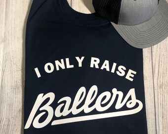 May include: A navy blue t-shirt with white text that reads "I only raise ballers" in a white, stylized font.