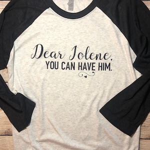 May include: A white and black baseball tee shirt with the text "Dear Jolene, You Can Have Him." printed on the front.