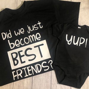 Peut inclure: Deux t-shirts noirs avec du texte blanc. Le plus grand t-shirt dit "Did we just become BEST FRIENDS?" Le plus petit t-shirt dit "yup!"