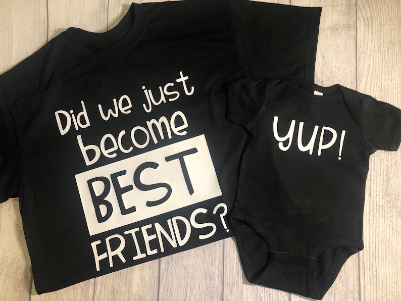 Peut inclure: Deux t-shirts noirs avec du texte blanc. Le plus grand t-shirt dit "Did we just become BEST FRIENDS?" Le plus petit t-shirt dit "yup!"