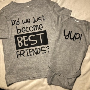 Peut inclure: Deux t-shirts gris avec du texte noir. Le plus grand t-shirt dit "Did we just become BEST FRIENDS?" Le plus petit t-shirt dit "Yup!"