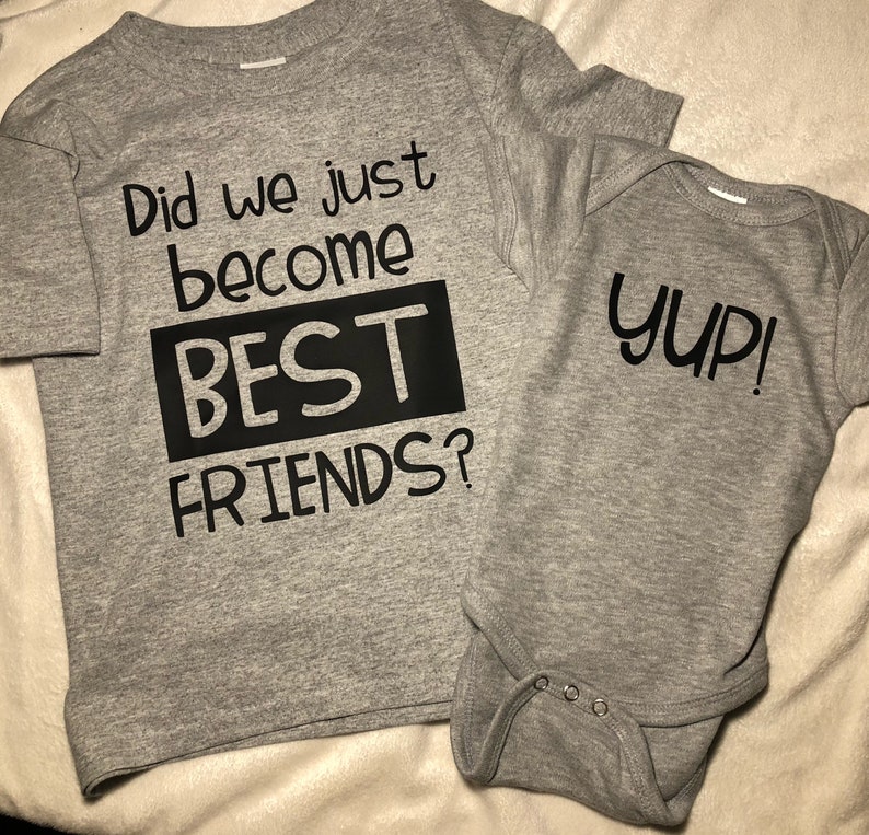 Peut inclure: Deux t-shirts gris avec du texte noir. Le plus grand t-shirt dit "Did we just become BEST FRIENDS?" Le plus petit t-shirt dit "Yup!"