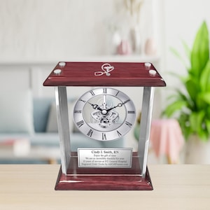 May include: A mahogany wood desk clock with a silver face and a glass front. The clock has a silver stethoscope design on the top and a personalized plaque with the text "Cindy J. Smith, RN Enjoy the gift of time We are so incredibly thankful for your 10 years of service at NYG Hospital Engraved Desk Clocks by A&CFrames.com".