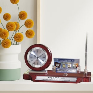May include: A mahogany desk clock set with a silver clock face, a pen holder, and a business card holder. The set has a personalized nameplate that reads "Rylie L. Walker, RN".