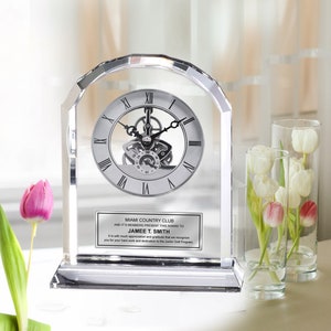May include: A clear crystal clock with a silver face and Roman numerals. The clock is on a base with a silver plaque that reads "Miami Country Club and it's members present this award to Jamee T. Smith. It is with much appreciation and gratitude that we recognize you for your hard work and dedication to the Junior Golf Program."