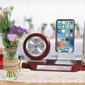 May include: A mahogany desk organizer with a clock, a phone stand, and a pen holder. The organizer has a personalized plaque that reads "Cindy McDaniel, MBA Engraved Desk Clocks by AllGiftIdeas.com Distributor of Recognition Clocks and Personalized Gifts".