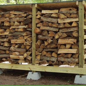 Puede incluir: Un estante de leña de madera con un techo verde, que se apoya en bloques de hormigón. El estante está lleno de leña apilada.