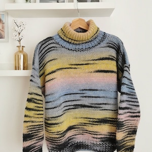 May include: A striped turtleneck sweater in shades of yellow, blue, black, and pink. The sweater is hanging on a wooden hanger.