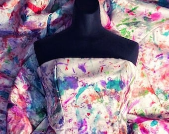 May include: A white strapless corset with a colorful abstract paint splatter design. The corset is on a mannequin and is surrounded by a white fabric with a similar paint splatter design.