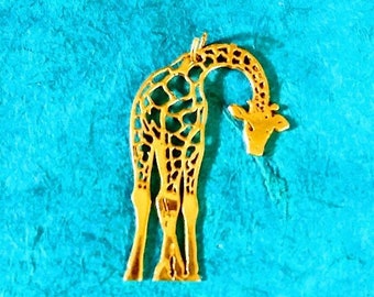 Puede incluir: Un colgante de jirafa de color dorado con un diseño de corte detallado. La jirafa está representada con la cabeza inclinada hacia abajo, como si estuviera mirando algo en el suelo.
