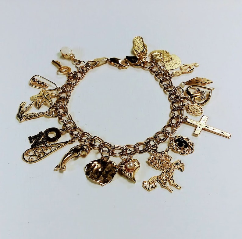 Pode incluir: Um bracelete de ouro com uma variedade de pingentes, incluindo um golfinho, um cora&ccedil;&atilde;o, uma cruz, um unic&oacute;rnio, uma concha, uma estrela do mar, uma chave e o n&uacute;mero "20".