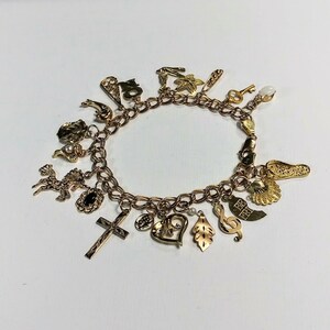 Pode incluir: Um bracelete de berloques de ouro com uma variedade de berloques, incluindo uma cruz, um cora&ccedil;&atilde;o, uma nota musical, uma folha, uma ferradura, uma chave, um sapato e um veado. Os berloques s&atilde;o feitos de ouro e t&ecirc;m detalhes intrincados.