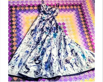 May include: A formal gown with a white base and a vibrant abstract pattern in shades of blue and teal. The dress features thin straps and a flowing skirt, creating an elegant silhouette. The fabric appears to be a lightweight material.