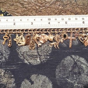Pode incluir: Um bracelete de charmes de ouro com uma variedade de charmes, incluindo uma chave, uma estrela, uma cruz, um cora&ccedil;&atilde;o, uma nota musical e uma concha. O bracelete &eacute; feito de metal dourado e tem um fecho de lagosta.