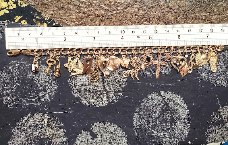 Pode incluir: Um bracelete de charmes de ouro com uma variedade de charmes, incluindo uma chave, uma estrela, uma cruz, um cora&ccedil;&atilde;o, uma nota musical e uma concha. O bracelete &eacute; feito de metal dourado e tem um fecho de lagosta.