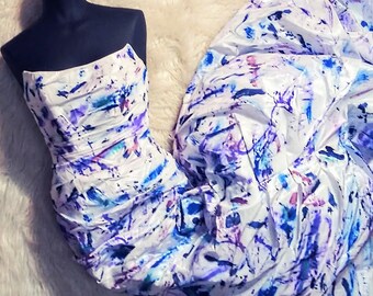 May include: A strapless white gown with a blue, purple, and pink abstract paint splatter design.