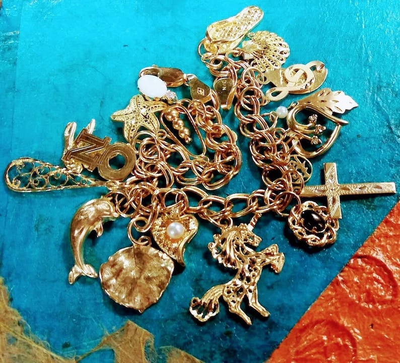 Pode incluir: Um bracelete de berloques de ouro com uma variedade de berloques, incluindo um golfinho, um unic&oacute;rnio, uma cruz, uma folha, um cora&ccedil;&atilde;o, uma estrela do mar, uma nota musical e um sapato. Os berloques est&atilde;o presos a uma corrente de ouro.