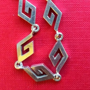 May include: Close-up of a silver chain necklace with a repeating pattern of interlocking geometric shapes.