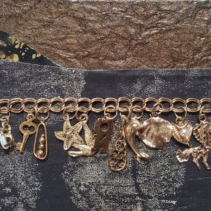 Pode incluir: Um bracelete de ouro com uma variedade de pingentes, incluindo uma chave, uma estrela do mar, uma concha, uma cruz e uma pequena pedra preta. O bracelete &eacute; feito de um estilo de corrente de elos.
