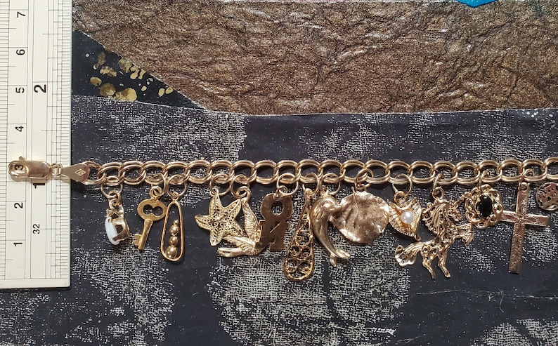 Pode incluir: Um bracelete de ouro com uma variedade de pingentes, incluindo uma chave, uma estrela do mar, uma concha, uma cruz e uma pequena pedra preta. O bracelete &eacute; feito de um estilo de corrente de elos.