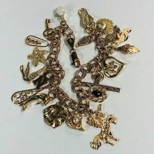 Pode incluir: Um bracelete de ouro com uma variedade de pingentes, incluindo um unic&oacute;rnio, um cora&ccedil;&atilde;o, uma cruz, uma chave, um p&aacute;ssaro, uma estrela do mar, uma folha e uma concha.