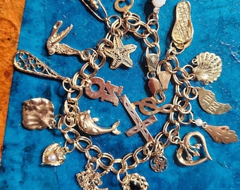May include: A gold charm bracelet with a variety of charms, including a dolphin, a starfish, a cross, a heart, a seashell, a key, a unicorn, a horseshoe, and a pair of flip flops.