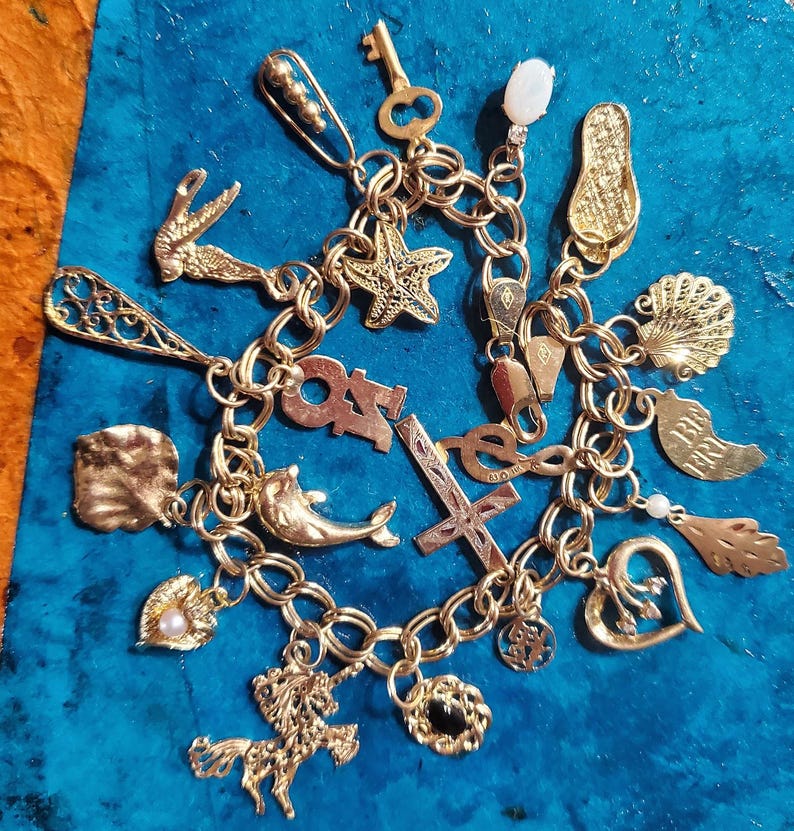 Pode incluir: Um bracelete de ouro com uma variedade de pingentes, incluindo um golfinho, uma estrela do mar, uma cruz, um cora&ccedil;&atilde;o, uma concha, uma chave, um unic&oacute;rnio, uma ferradura e um par de chinelos.