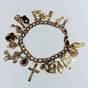 Pode incluir: Um bracelete de ouro com uma variedade de pingentes, incluindo uma cruz, um cora&ccedil;&atilde;o, uma nota musical, um p&aacute;ssaro, uma estrela, uma chave, um sapato e um cavalo. O bracelete &eacute; feito de uma corrente de ouro com um fecho de lagosta.