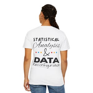 May include: White t-shirt featuring the text "STATISTICAL Analysis & DATA Reconfiguration" in black script and block letters, with colourful dots. A casual wear item.