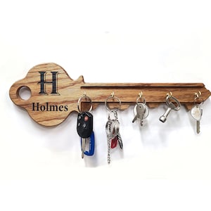 May include: Wooden key-shaped wall-mounted key holder with five hooks. The holder is engraved with the letter "H" and the name "Holmes".