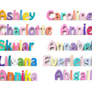 Puede incluir: Una colecci&oacute;n de diez nombres personalizados formados por letras de madera individuales y aut&oacute;nomas. Cada letra presenta un acabado mate suave en una variedad de colores pastel y vibrantes, incluyendo rosa, morado, azul, amarillo, naranja y verde azulado.