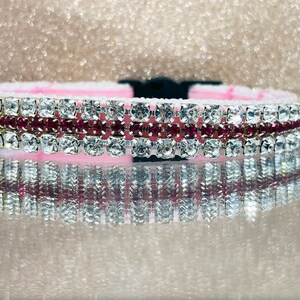 May include: A pink and silver dog collar with multiple rows of clear and pink rhinestones.