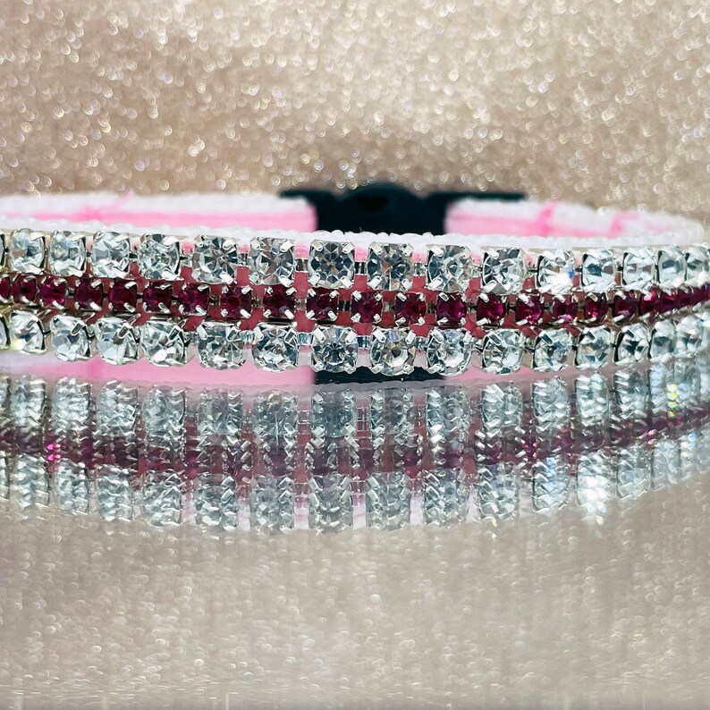 May include: A pink and silver dog collar with multiple rows of clear and pink rhinestones.