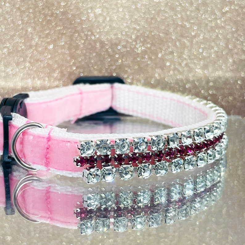 May include: Pink velvet dog collar with a white trim and a row of clear and pink rhinestones.