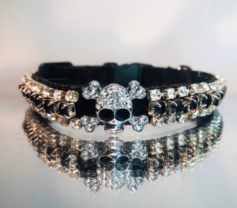Pode incluir: Coleira de veludo preto para animais de estima&ccedil;&atilde;o com um amuleto de caveira e ossos cruzados de prata adornado com strass transparentes. A coleira &eacute; adornada com fileiras de strass transparentes e pretos.
