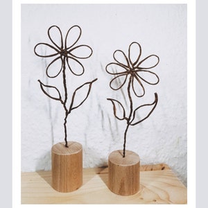 Könnte beinhalten: Zwei Draht-Skulpturen von Blumen mit braunen Stielen und Blättern, die auf Holzsockeln stehen.