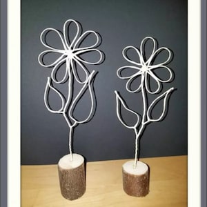 Könnte beinhalten: Zwei weiße Drahtskulpturen von Blumen mit Holzsockeln. Die Blumen sind stilisiert und haben jeweils fünf Blütenblätter.