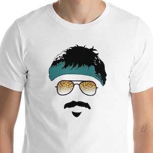 Puede incluir: Camiseta blanca con una ilustración en blanco y negro de una persona con gafas de sol y un pañuelo turquesa con estampado de leopardo.