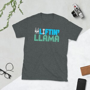 May include: A dark heather grey t-shirt with a blue and white graphic of a llama wearing sunglasses and holding a dumbbell. The text "Liftin' Llama" is printed in blue and white.