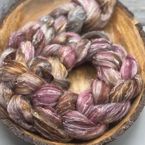 Könnte beinhalten: Ein geflochtenes Garnbündel in Braun-, Rosa- und Weißtönen. Das Garn ist kreisförmig angeordnet und befindet sich in einer Holzschale.